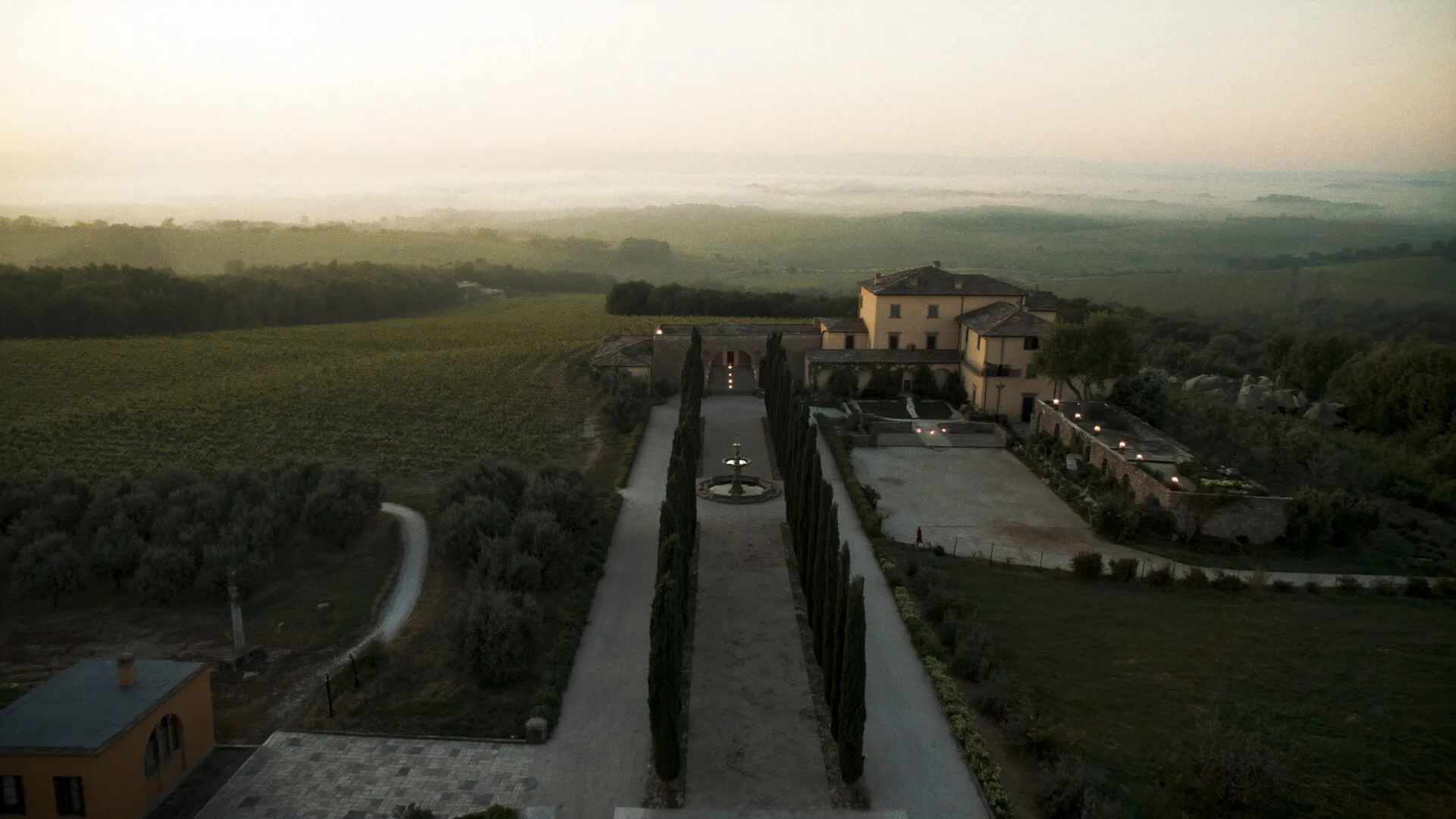 Tuscan vineyard estate at dusk, cypress-lined avenue leading to a stone villa